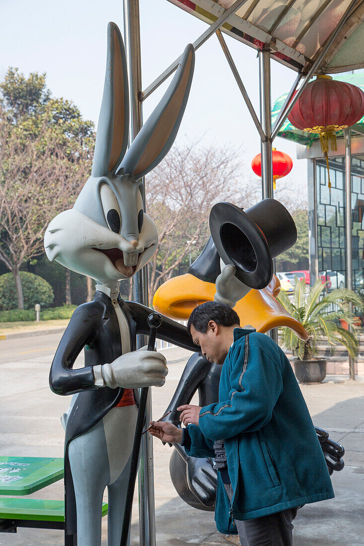 Mann gibt einer Bugs Bunny Figur in einem Vergnügunspark einen neuen Anstrich, Shanghai, China, Asien
