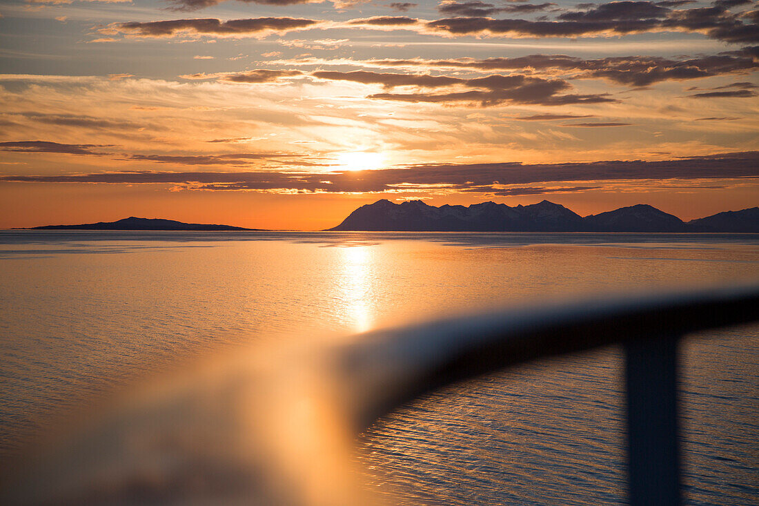 Deck railing of cruise ship MS Deutschland (Reederei Peter Deilmann) with coastline and mountains at sunset, near Lofoten, Norway