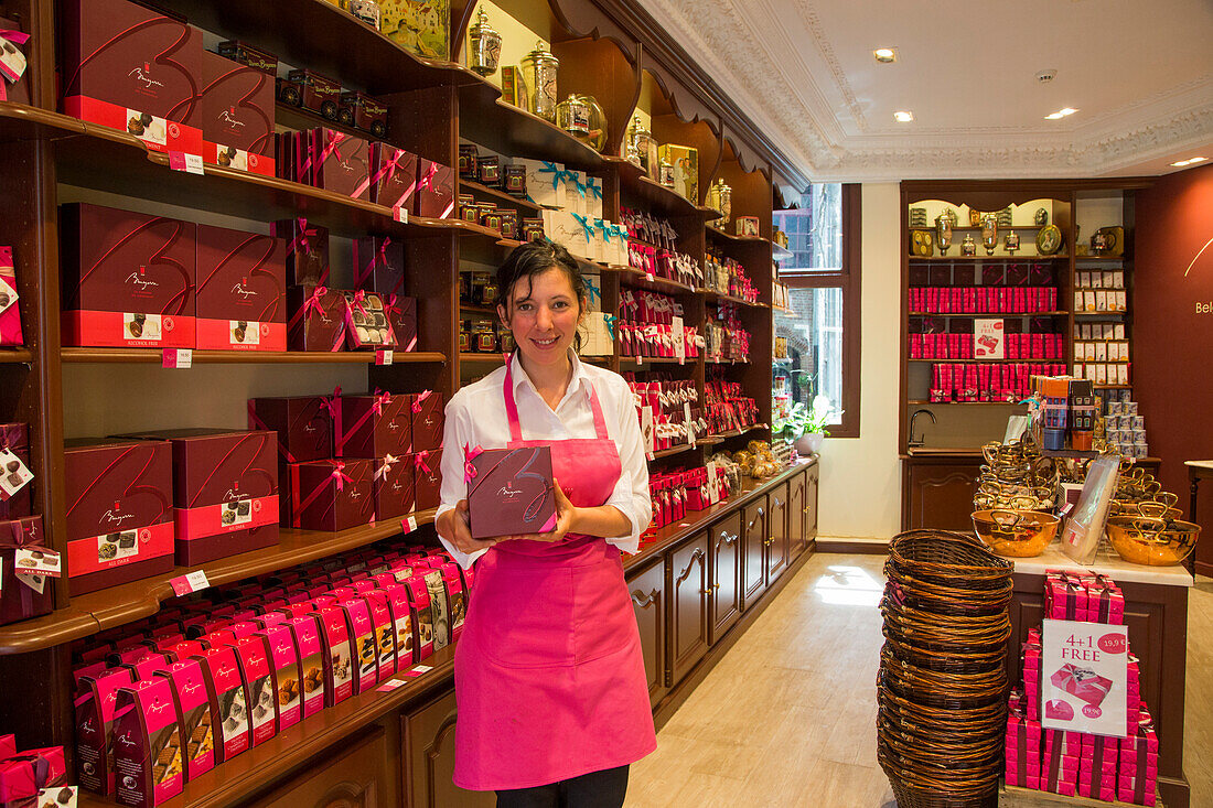 Friendly saleswomen displays chocolates for sale at Brugerren chocholate shop, Bruges (Brugge), Flemish Region, Belgium