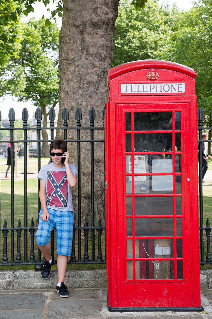Teenager mit Mobiltelefon steht neben roter Telefonzelle, Greenwich, London, England, Großbritannien, Europa