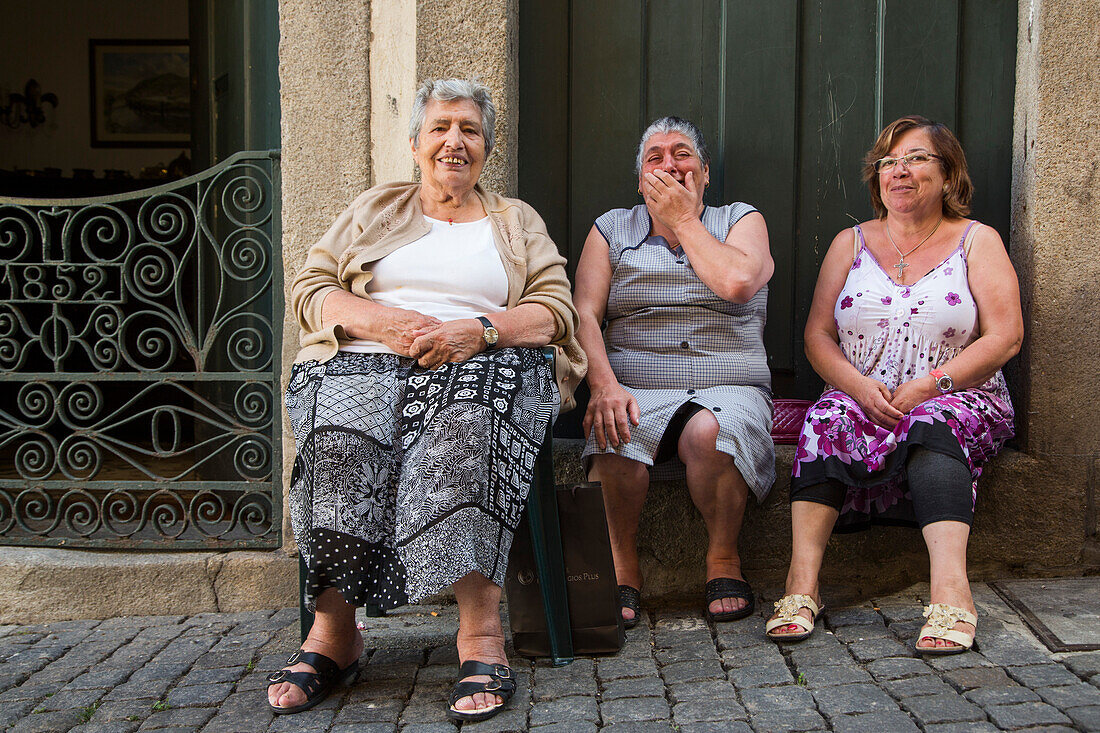 Three elderly women sit in alley and laugh heartily in Ribeira old town and historical center, Porto, Norte, Portugal