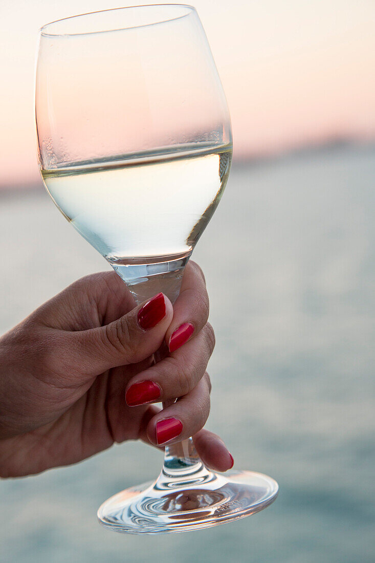 Hand einer Frau mit roten Fingernägeln hält Weißweinglas an Bord von Kreuzfahrtschiff MS Deutschland (Reederei Peter Deilmann) im Mittelmeer, nahe La Goulette, Tunis, Tunesien, Afrika