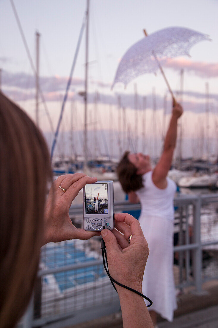 Frau fotografiert Freundin die einen Regenschirm in die Luft hält an der Larnaca Marina in der Abenddämmerung, Larnaka, Larnaca, Zypern, Europa