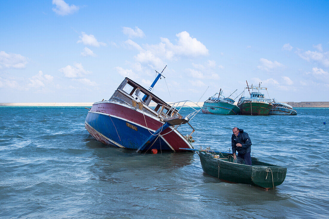 Fisherman in dinghy near capsized fishing boats in Crotone harbor, Crotone, Calabria, Italy