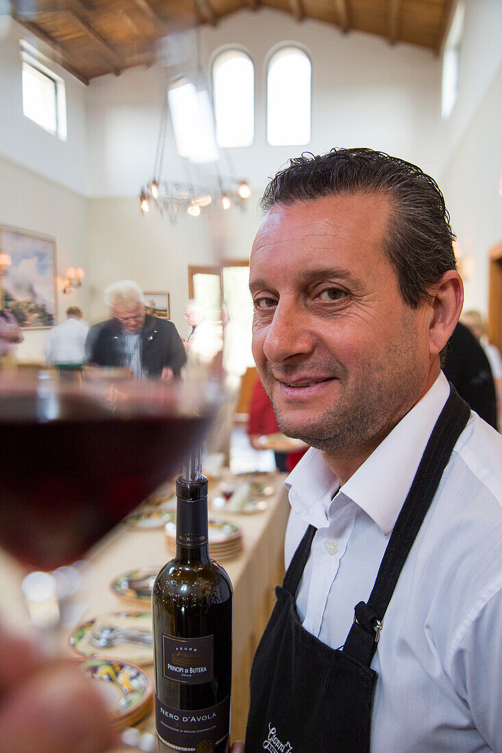 Waiter with wine bottle during winetasting at Feudo Principi di Butera winery, Deliella, near Butera, Sicily, Italy