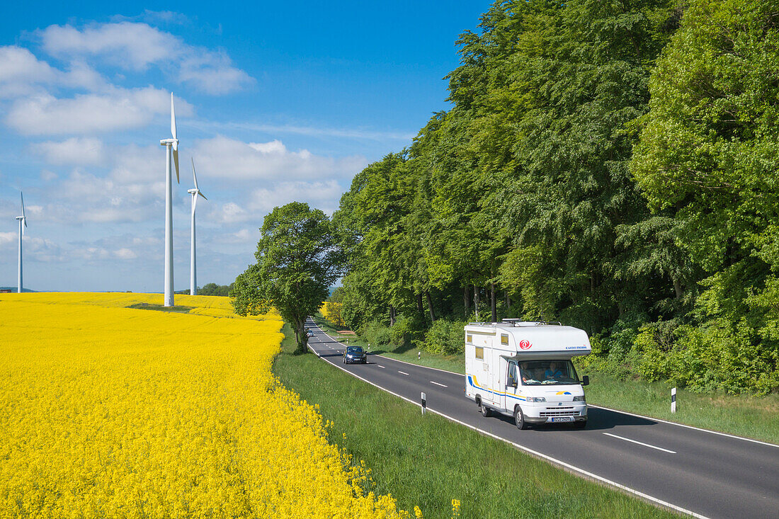 Wohnmobil auf Bundesstraße B62 und Windräder inmitten von blühenden Rapsfeldern, nahe Alsfeld, Vogelsberg, Hessen, Deutschland, Europa