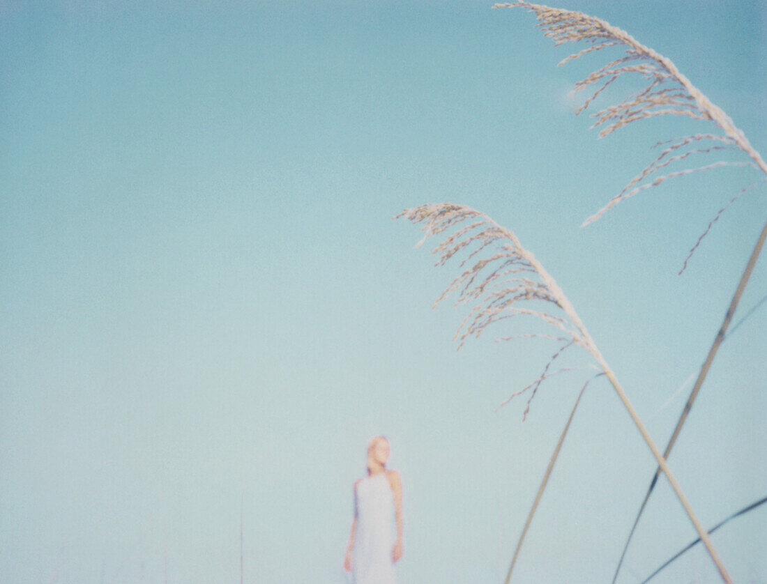 Woman standing in the distance, focus on tall grass in foreground