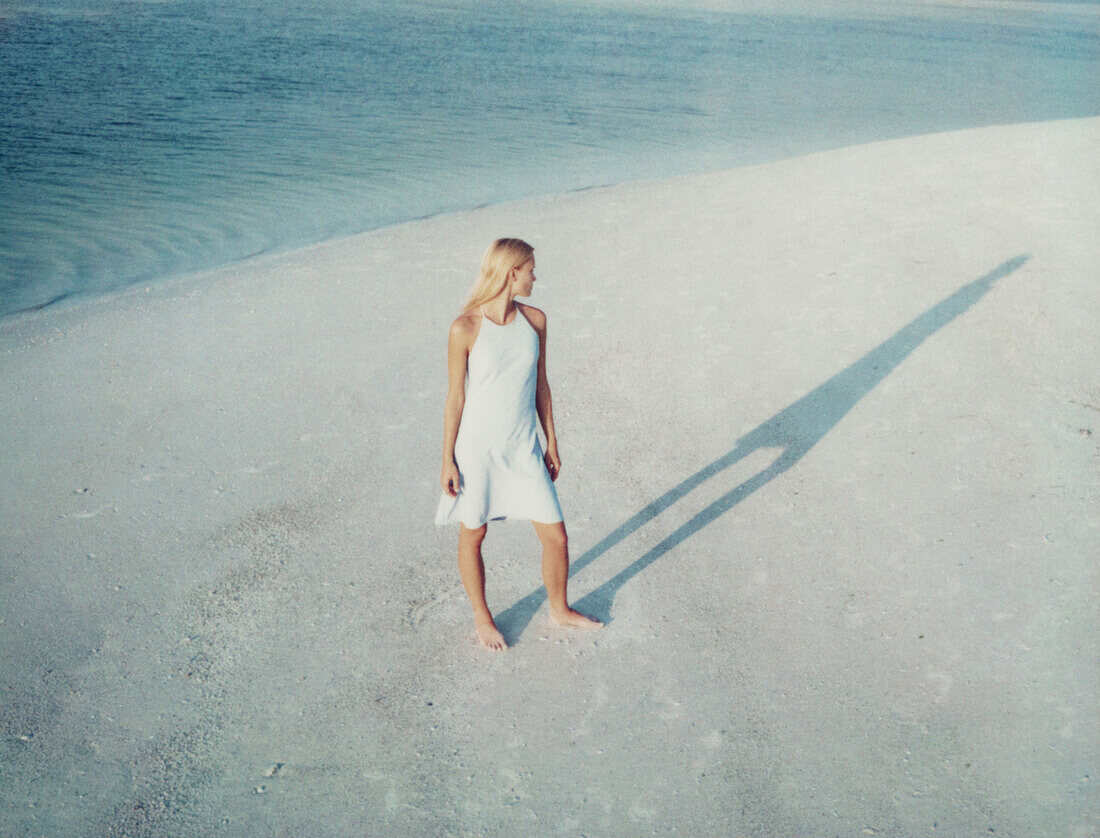 Frau am Strand stehend und ihren Schatten betrachtend