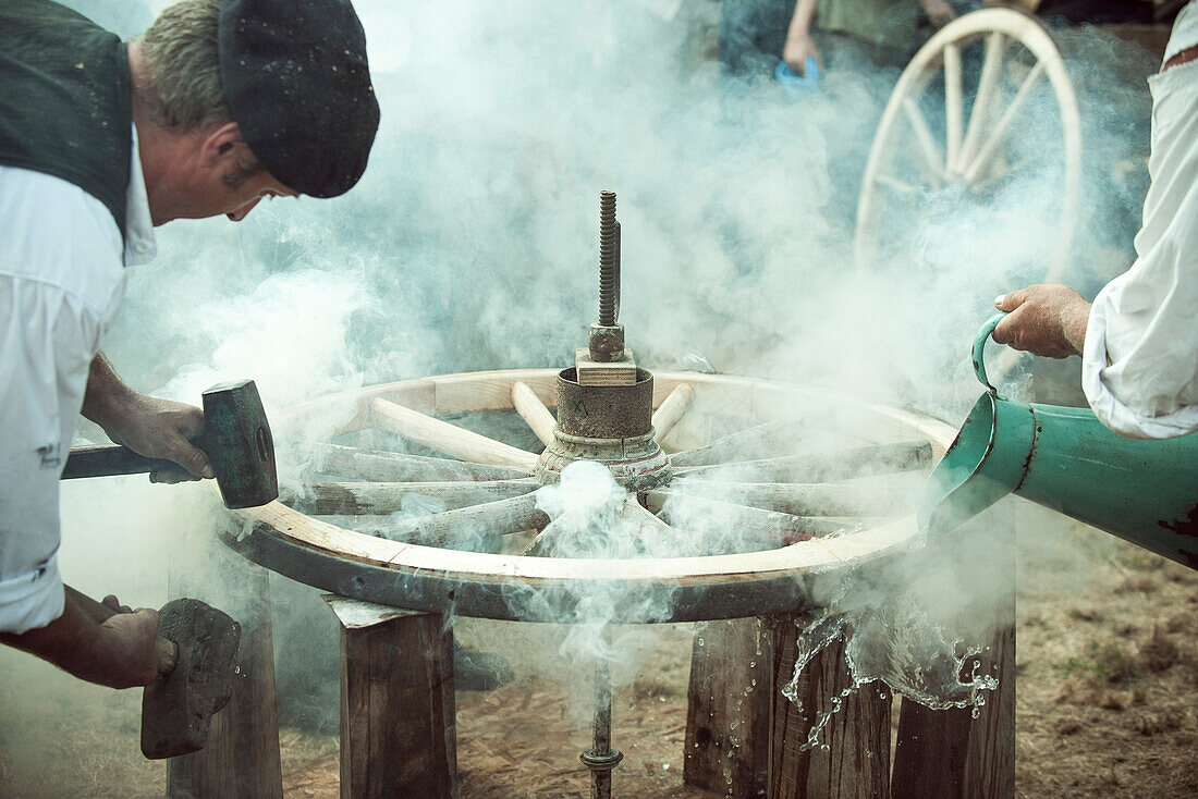 Craftsmen repairing horse-drawn wagon wheel