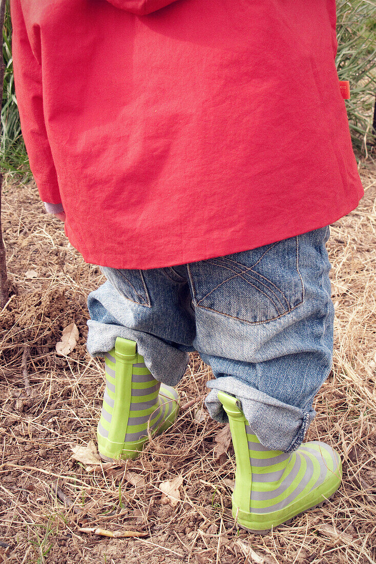 Child wearing raincoat and rubber boots, cropped