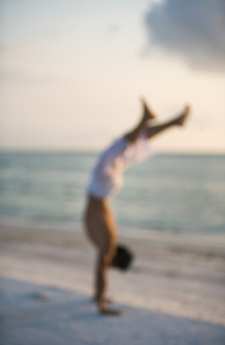 Man doing handstand on beach at sunrise, defocused