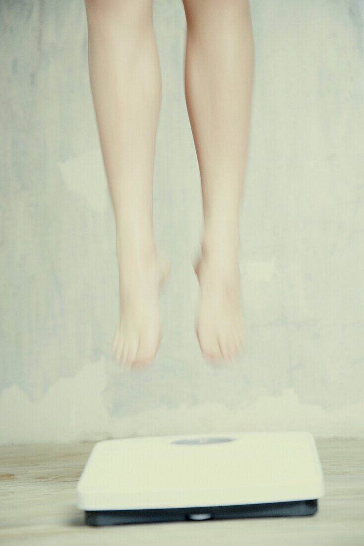 Woman's legs floating above bathroom scale