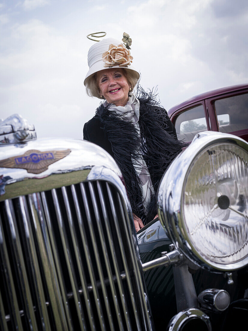 Besucherin freut sich über den passenden Hut zum Lagonda Familienerbstück, Goodwood Revival 2014, Rennsport, Autorennen, Classic Car, Goodwood, Chichester, Sussex, England, Großbritannien