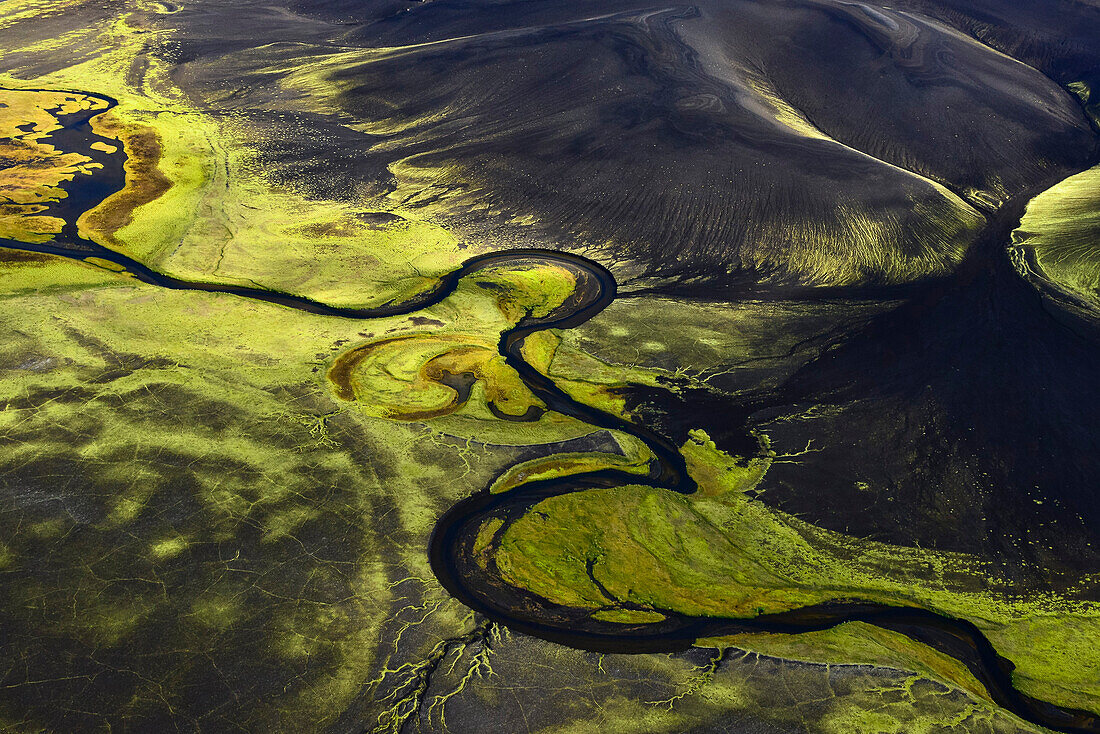 Aerial view of a surreal river valley with volcanic dark mountains covered with neon  patterns of fluorescent mosses, Veidivotn, Highlands, South Iceland, Iceland, Europe