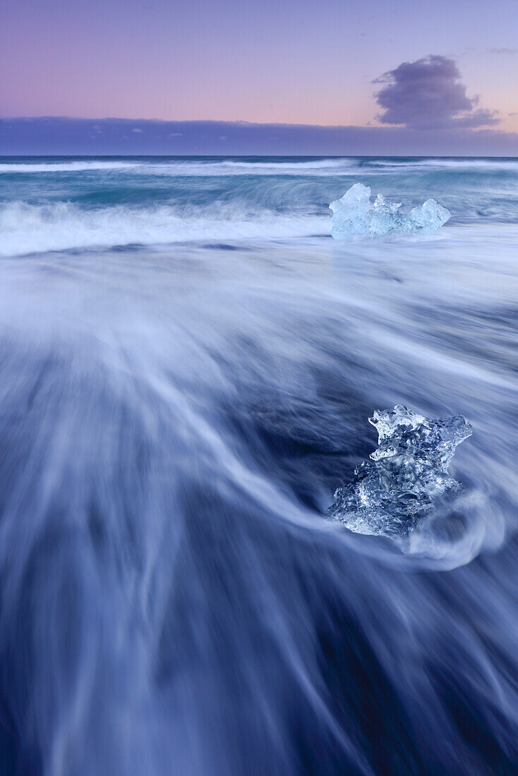 Eisblöcke bei Sonneuntergang an schwarzem Lavastrand, die vom Gletschersee Jökulsarlon  am Vatnajökull-Gletscher angespült werden, Breidamerkursandur zwischen dem Skaftafell-Nationalpark und Höfn, Ostisland, Island, Europa