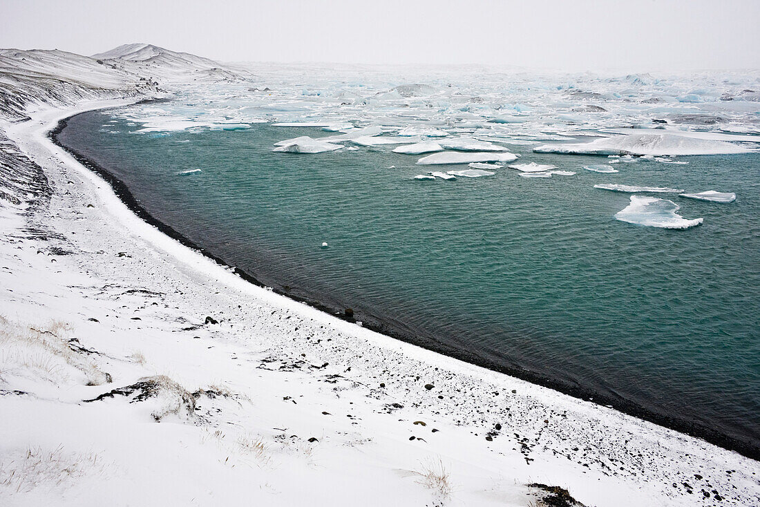 Gletschersee Jökulsarlon mit Eisbergen und verschneitem Ufer am Vatnajökull, Breiðamerkursandur zwischen dem Skaftafell-Nationalpark und Höfn, Ostisland, Island, Europa