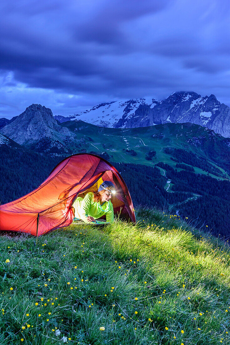 Frau sitzt in erleuchtetem Zelt, Marmolada im Hintergrund, Sellagruppe, UNESCO Weltnaturerbe Dolomiten, Dolomiten, Trentino, Italien