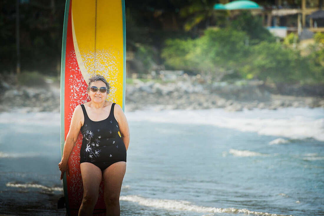 Older Hispanic woman with surfboard on beach, Sayulita, Nayarit, Mexico