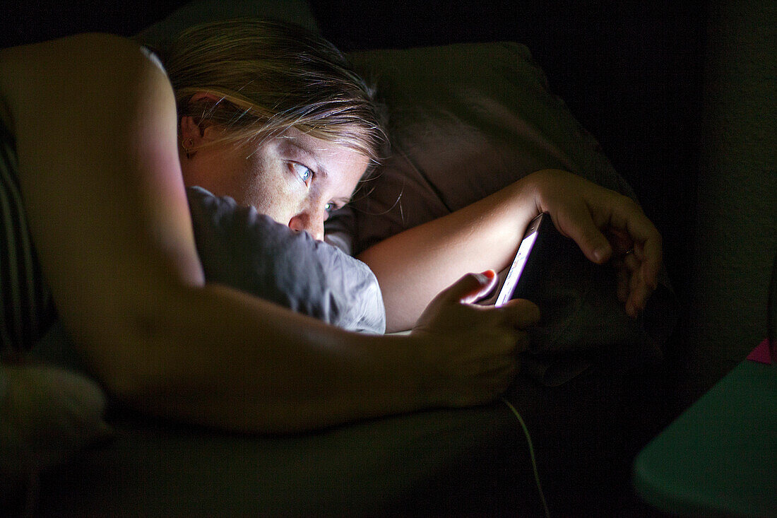 Caucasian woman using cell phone in bed, Oakland, California, United States