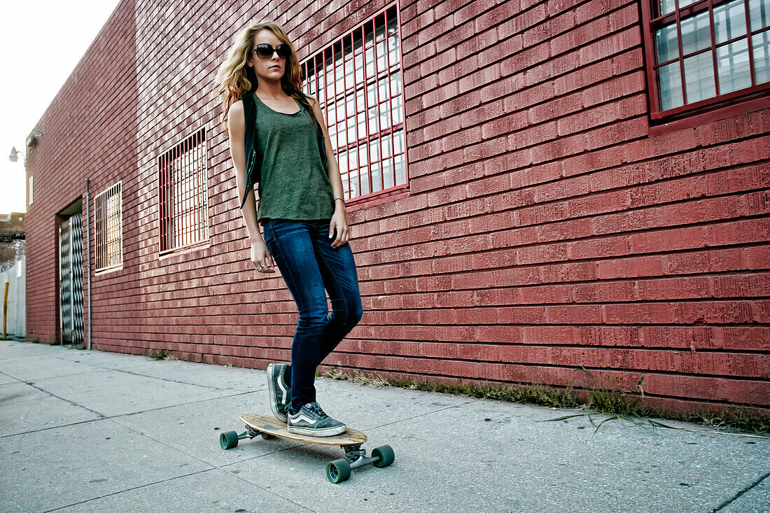 Mixed race woman riding skateboard on city street, Los Angeles, California, USA