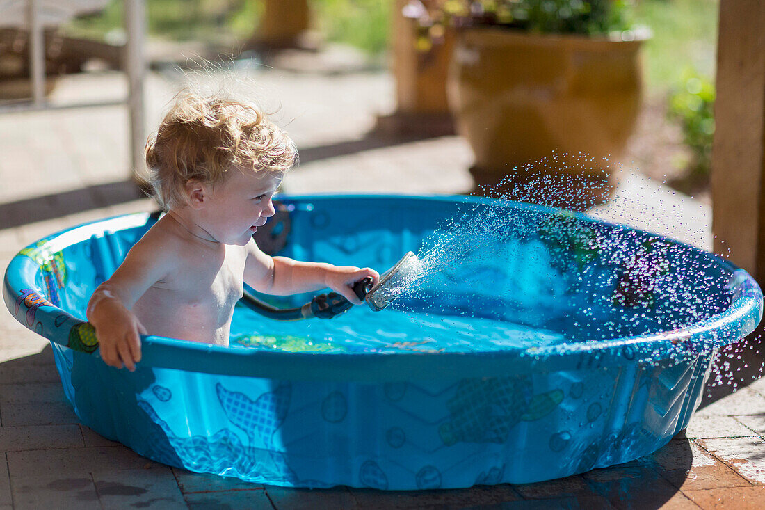 Caucasian baby playing with hose in wading pool, Santa Fe, New Mexico, USA