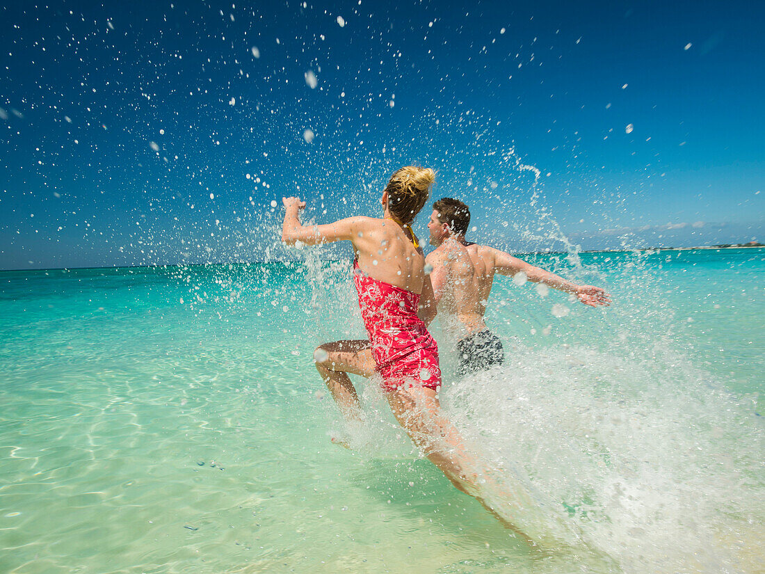 Caucasian couple splashing in waves in tropical ocean, C1