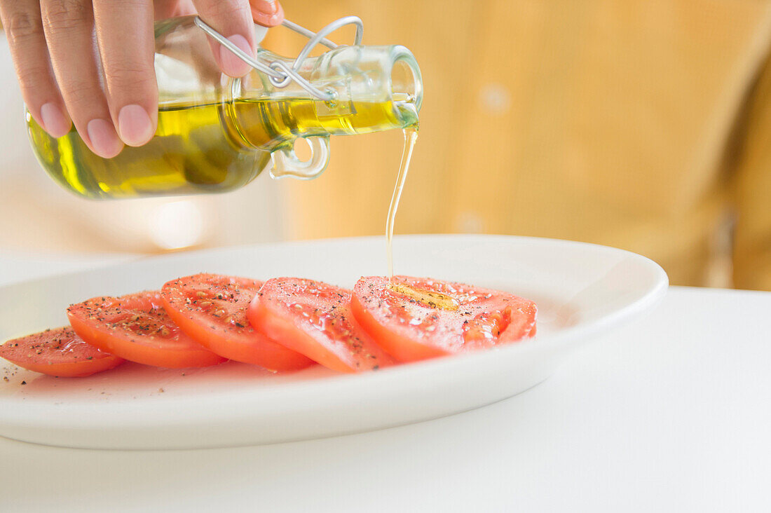 Close up of mixed race man pouring oil on tomatoes, C1