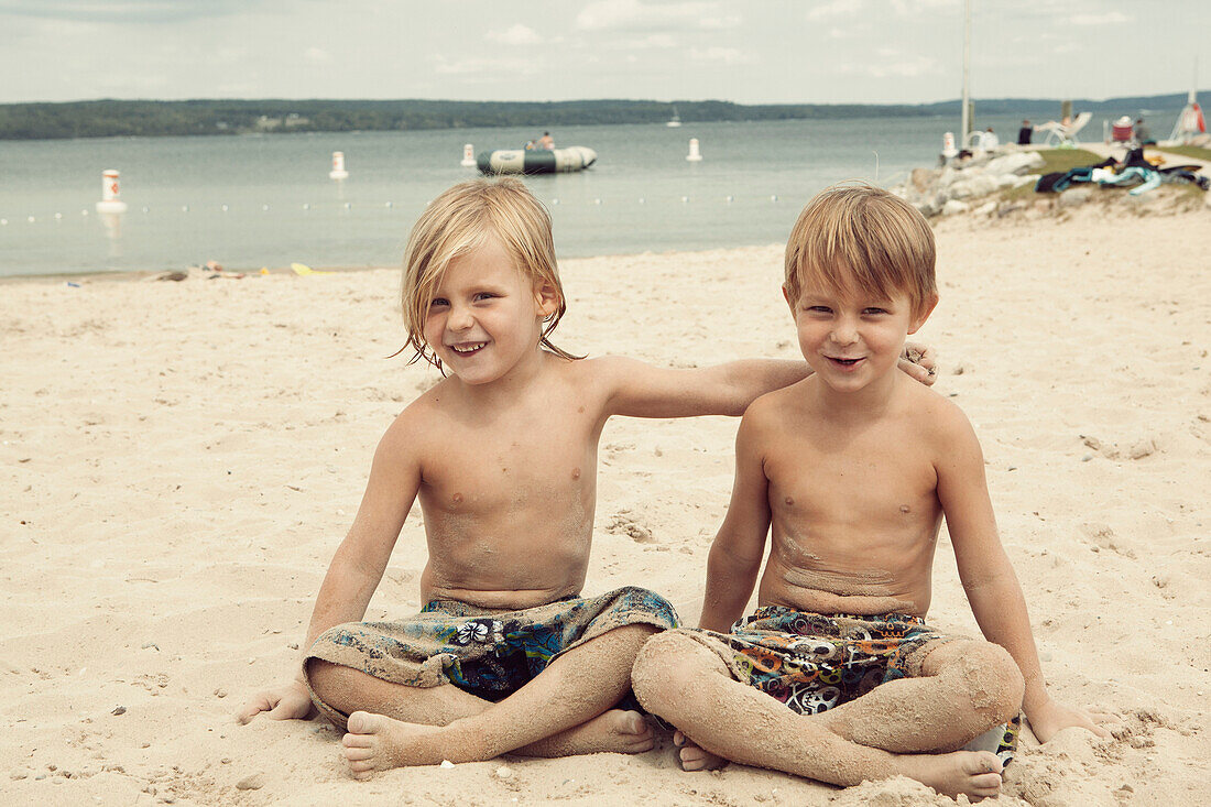 Caucasian brothers hugging on beach, C1