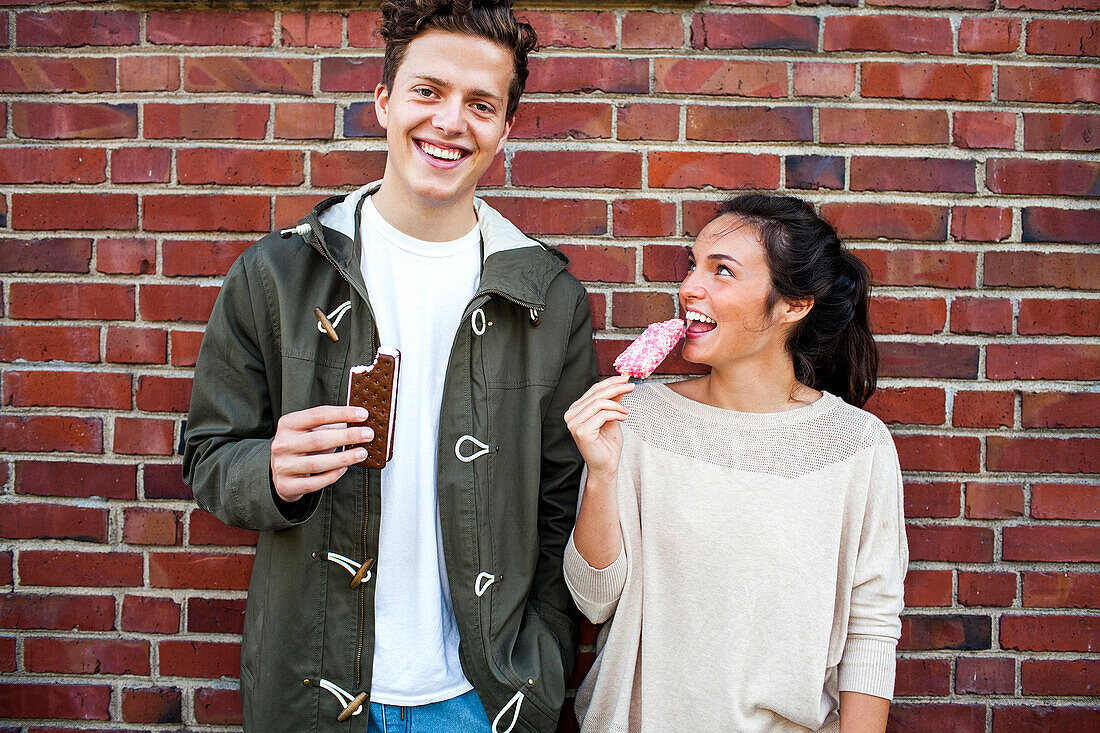 Caucasian couple eating ice cream near red brick wall, Seattle, Washington, United States
