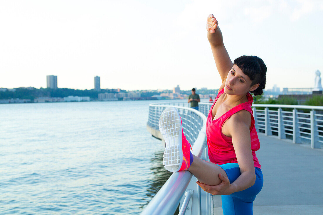 Mixed race woman stretching on urban waterfront railing, , NYC, NY, USA