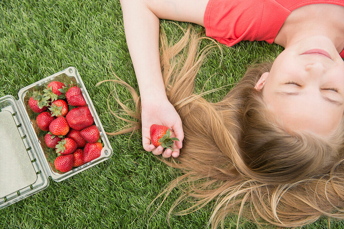 Caucasian girl holding strawberries on grassy lawn, Jersey City, New Jersey, USA