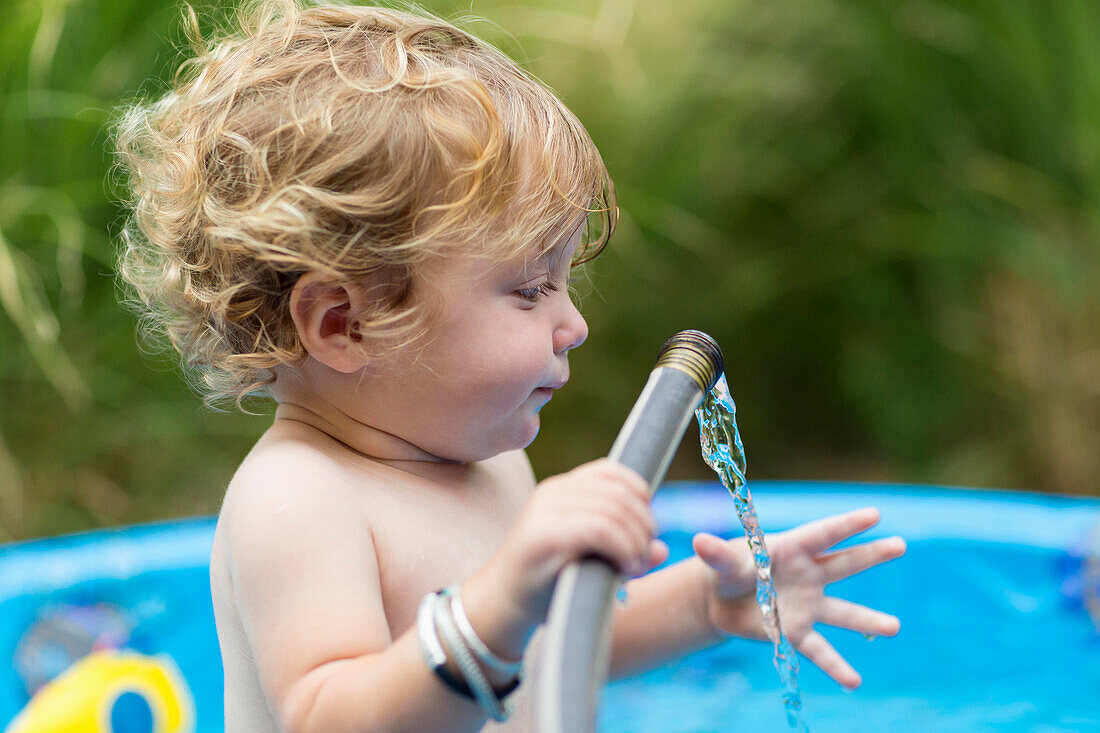 Caucasian baby boy playing with hose in swimming pool, Santa Fe, New Mexico, USA