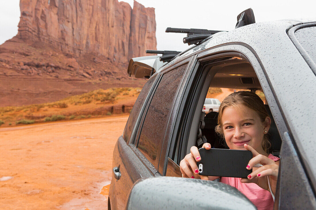 Caucasian girl taking cell phone photograph from car, Monument Valley, Utah, United States, Monument Valley, Utah, USA
