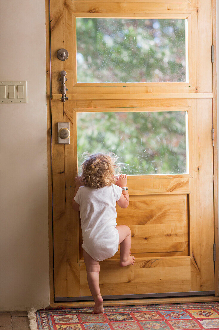 Caucasian baby boy peering out door window, Santa Fe, New Mexico, USA