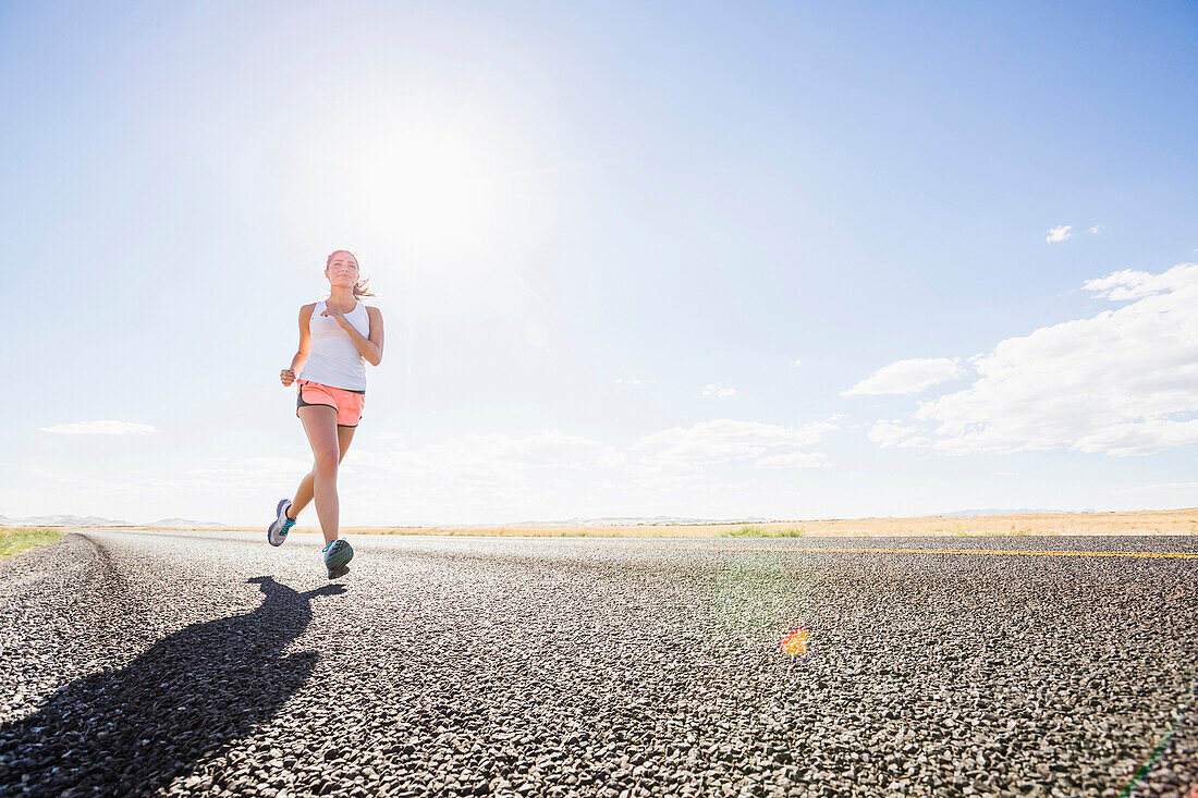 Caucasian woman running on remote road, Little Sahara, Utah, USA