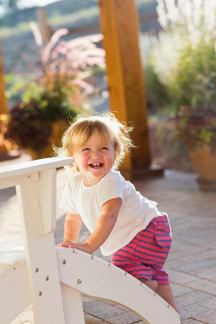 Caucasian baby boy climbing adirondack chair on patio, Santa Fe, New Mexico, USA