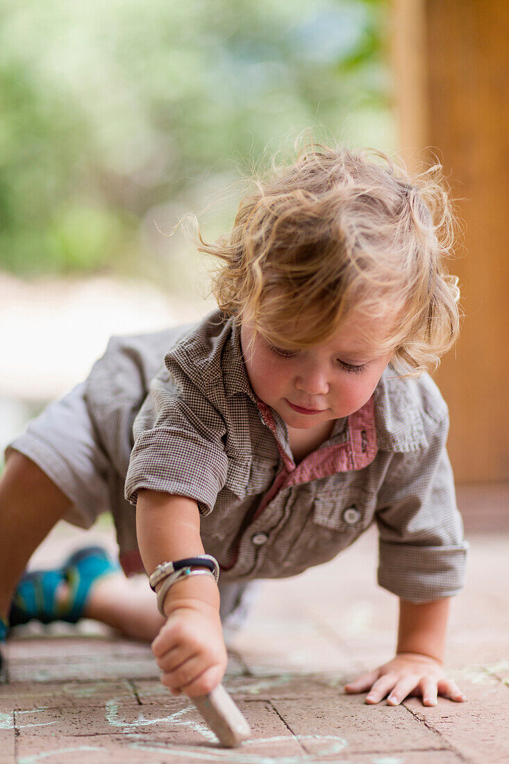 Caucasian baby boy drawing with chalk on brick patio, Santa Fe, New Mexico, USA