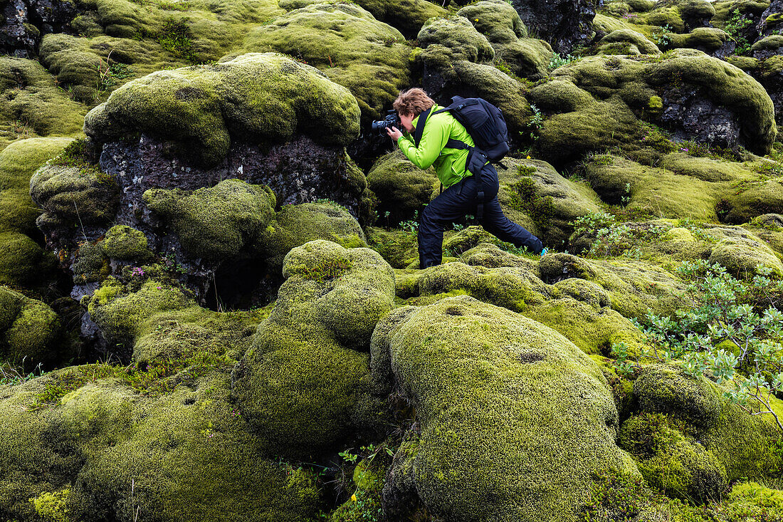 Hiker taking photograph on mossy rock formations, Southern Iceland, Southern Iceland, Iceland