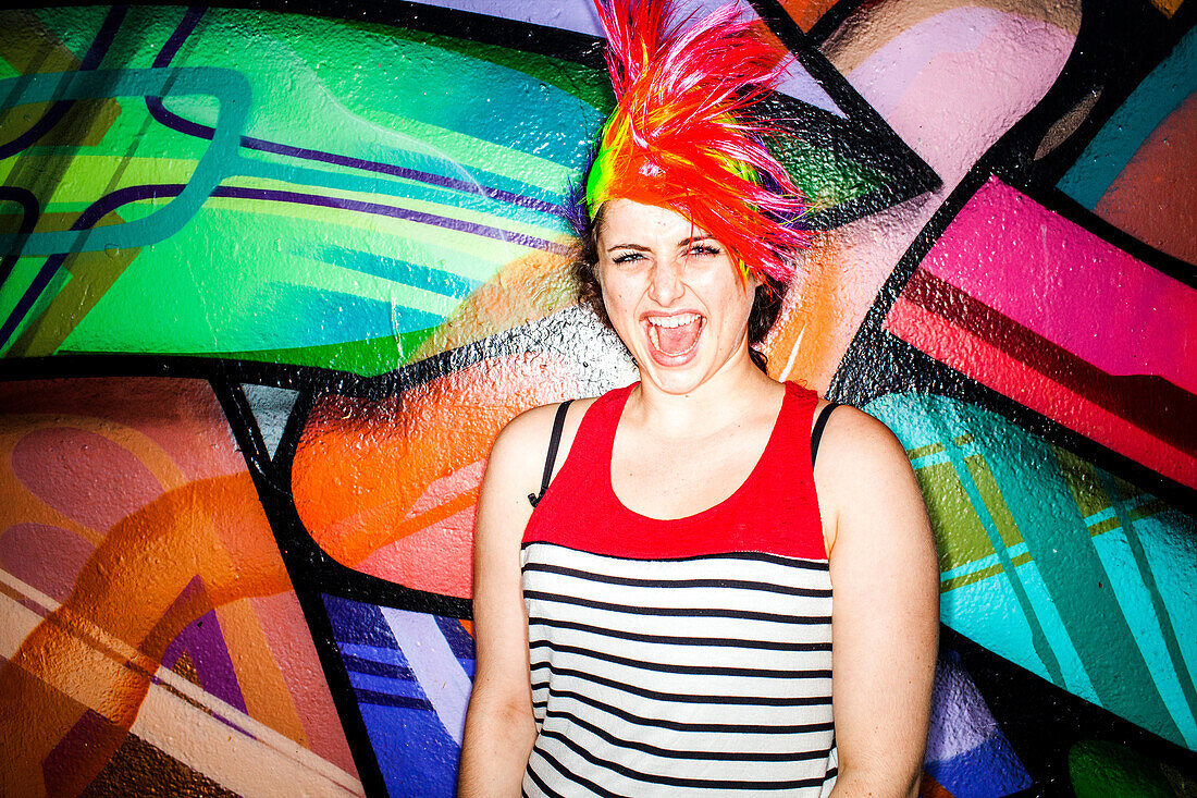Caucasian woman in colorful wig laughing near graffiti wall, San Francisco, California, United States
