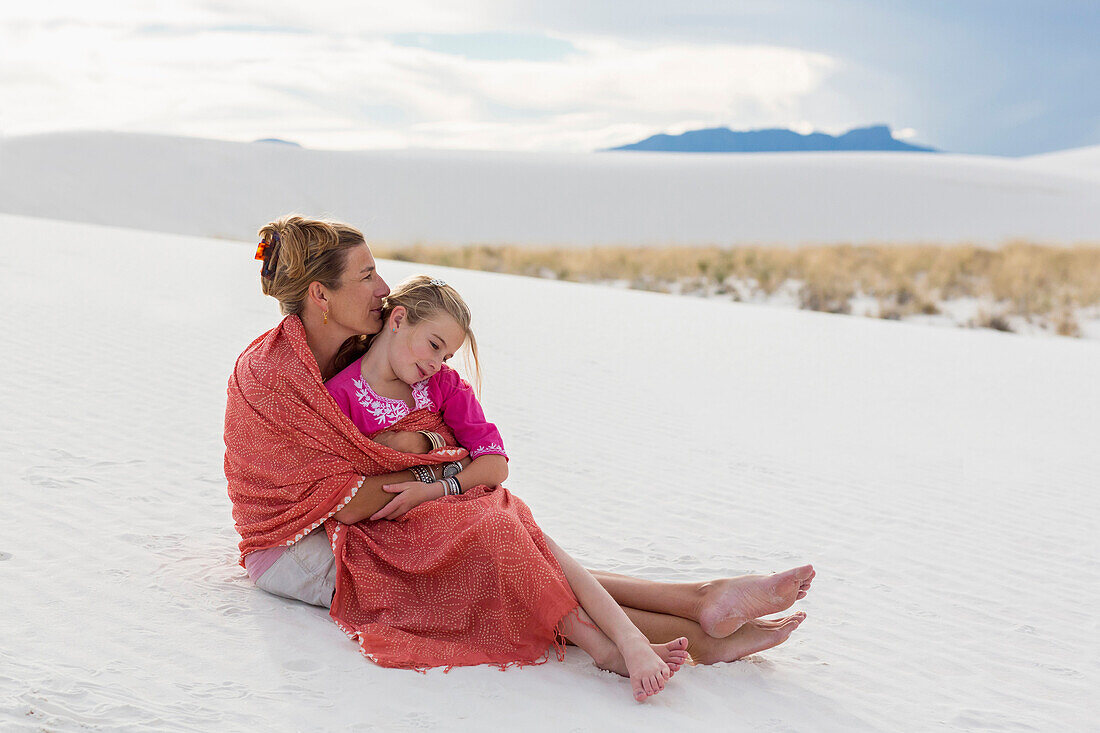 Caucasian mother and daughter wrapped in blanket on sand dune, White Sands, New Mexico, USA