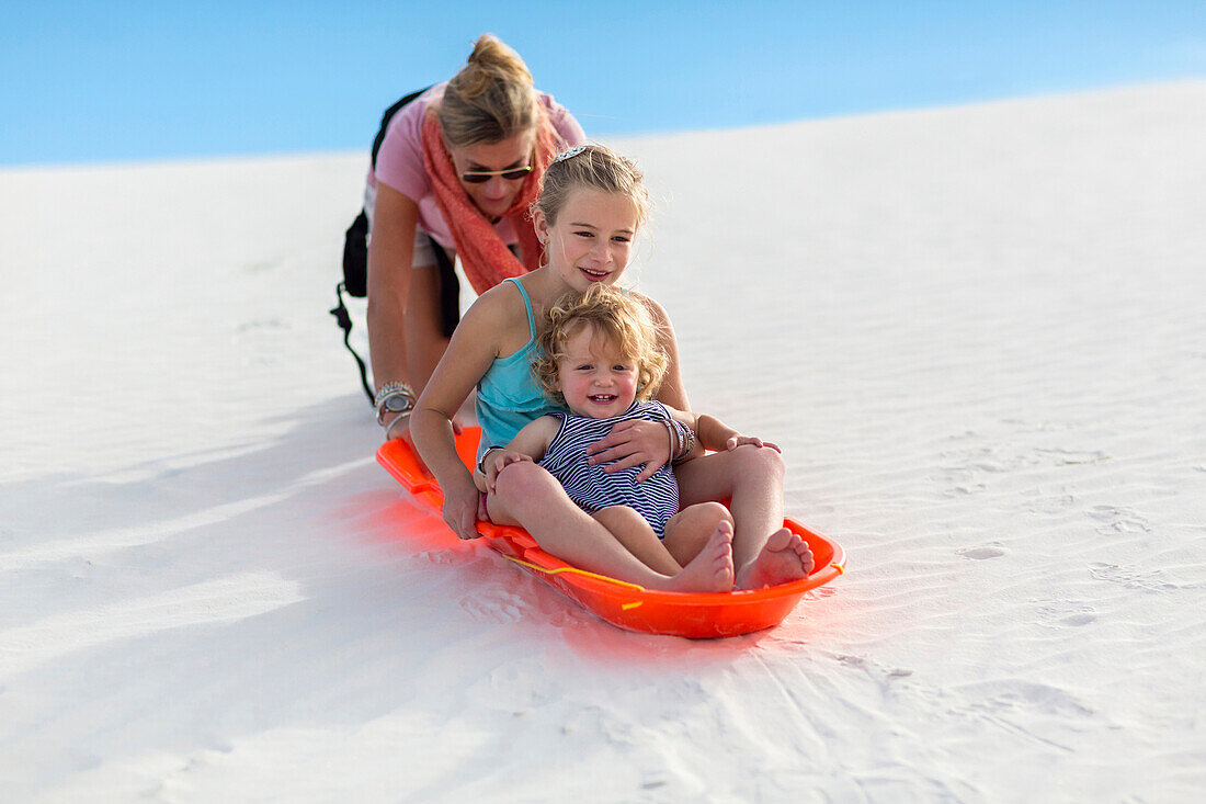 Caucasian mother and children sledding on sand dune, White Sands, New Mexico, USA
