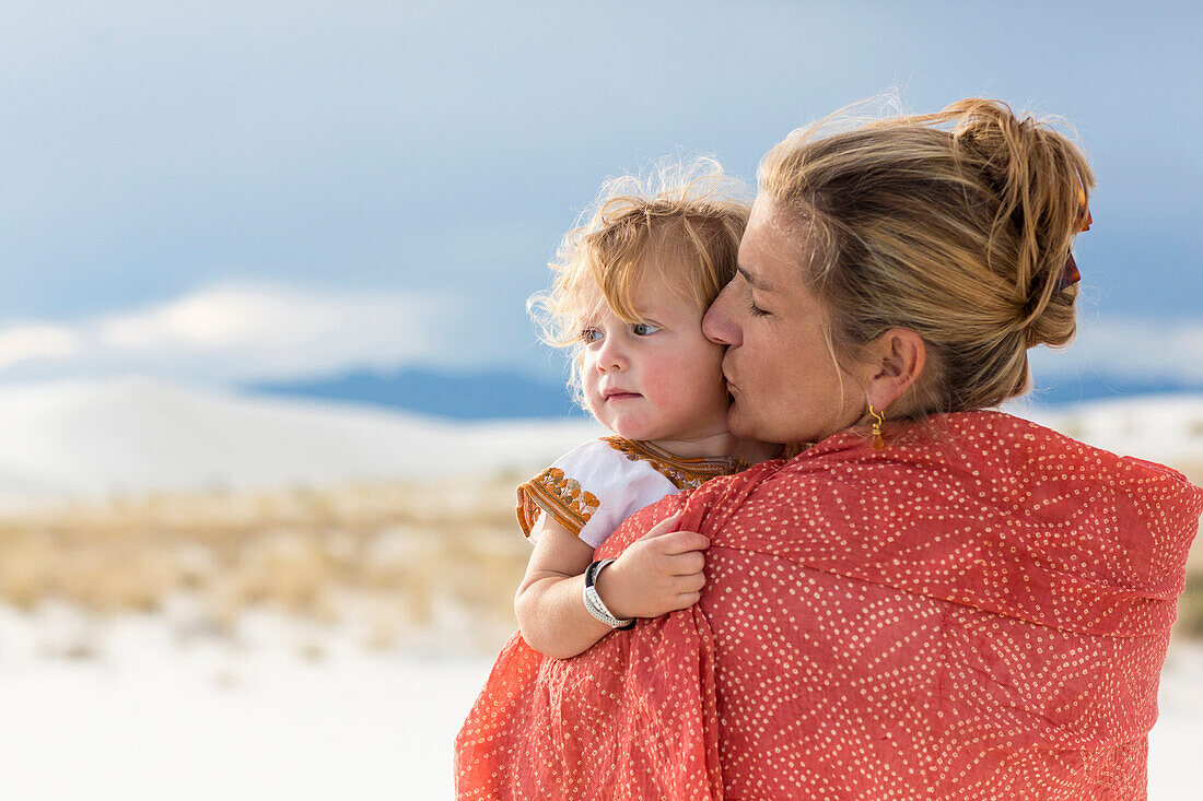 Caucasian mother and son wrapped in blanket on sand dune, White Sands, New Mexico, USA