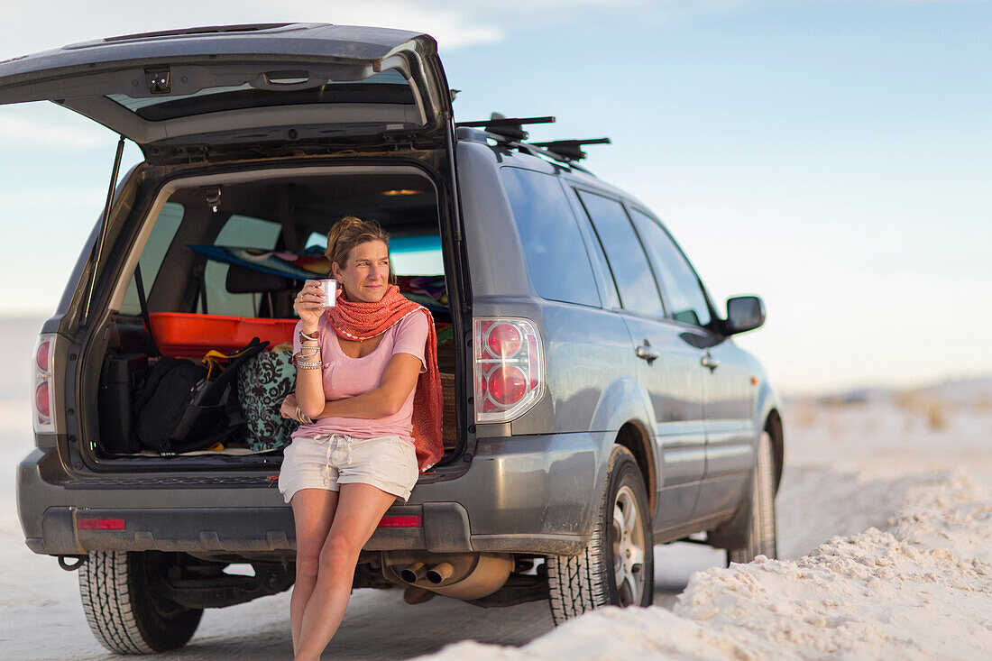 Caucasian woman leaning on car drinking coffee, White Sands, New Mexico, USA