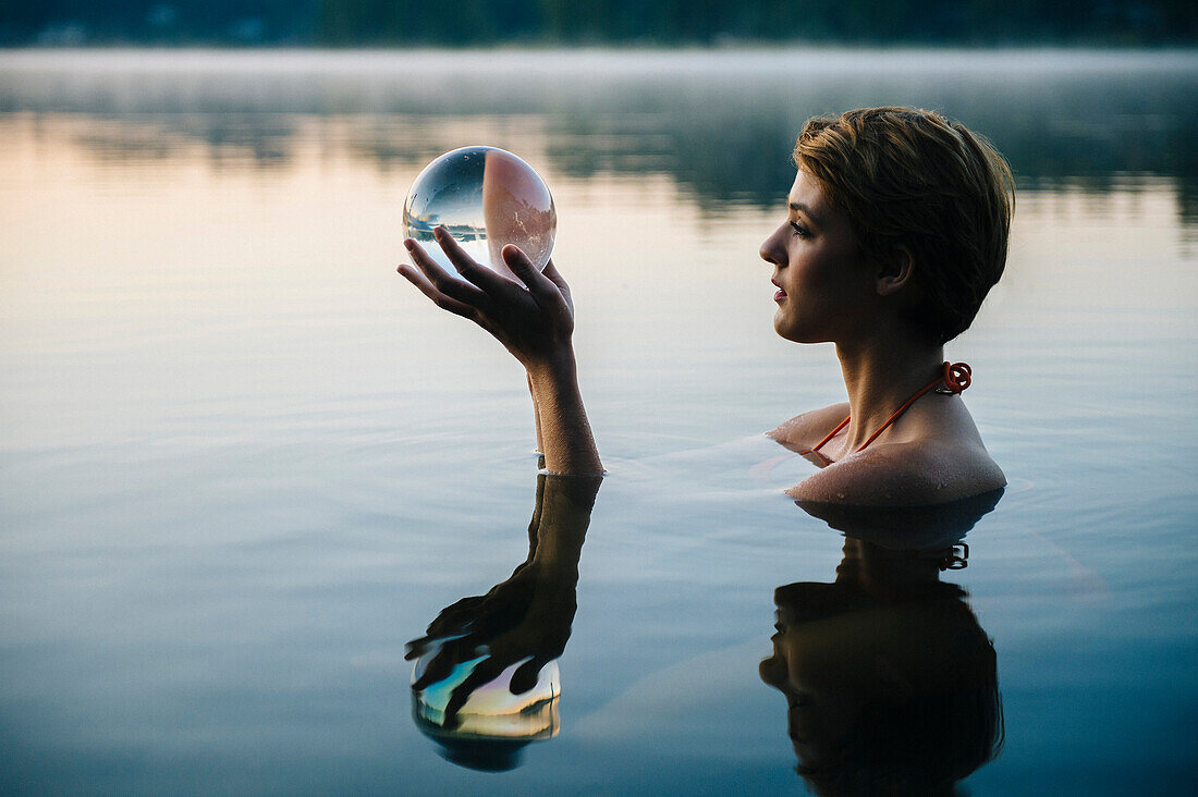 Caucasian woman holding crystal ball in still lake, Bremerton, Wa, USA