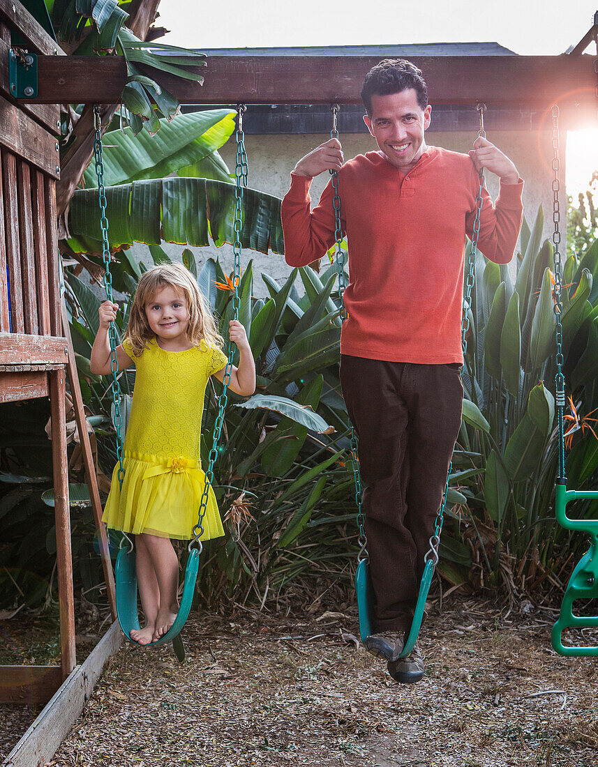 Caucasian father and daughter standing on swings, Los Angeles, California, USA