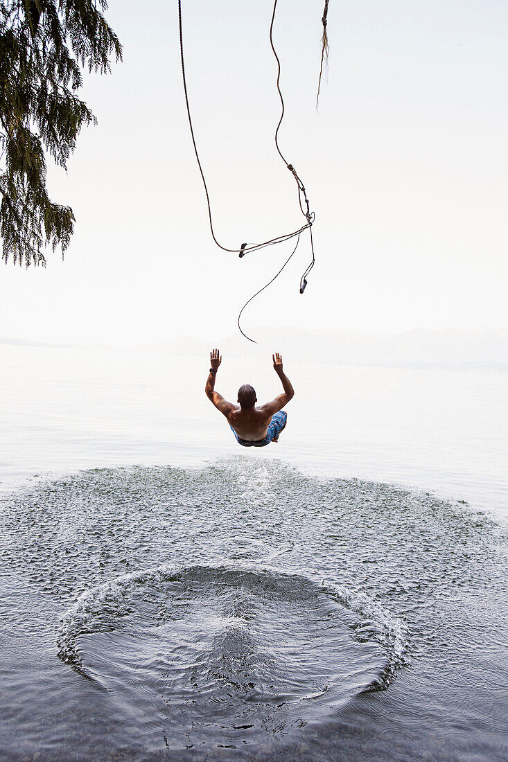 Man jumping from rope swing into lake, Hope, Idaho, USA