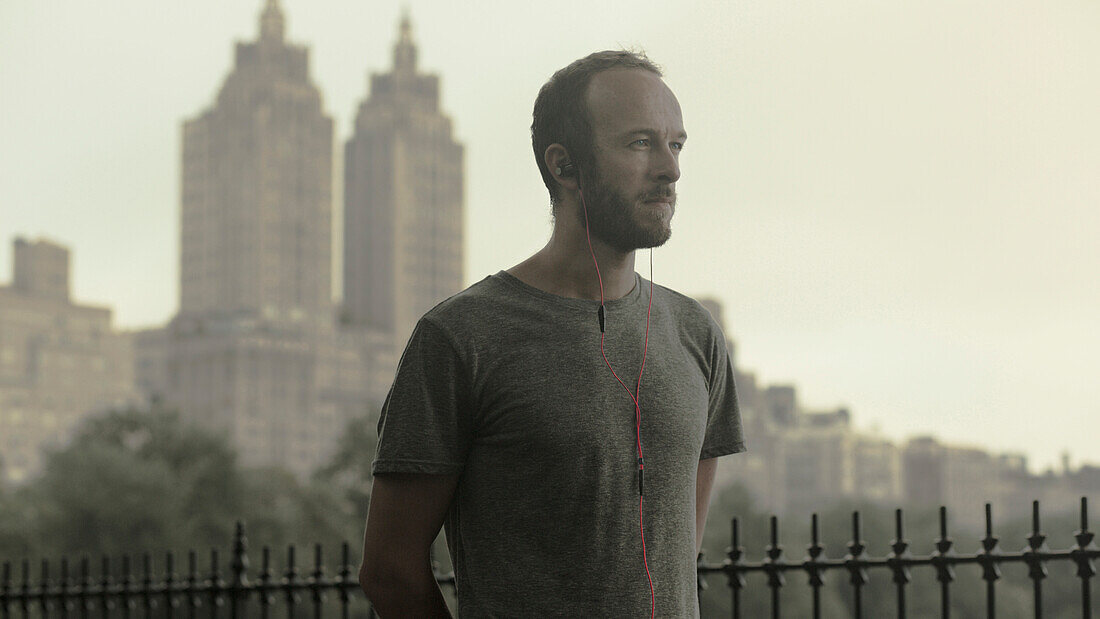 Caucasian runner listening to earbuds in front of city skyline, New York, New York, USA