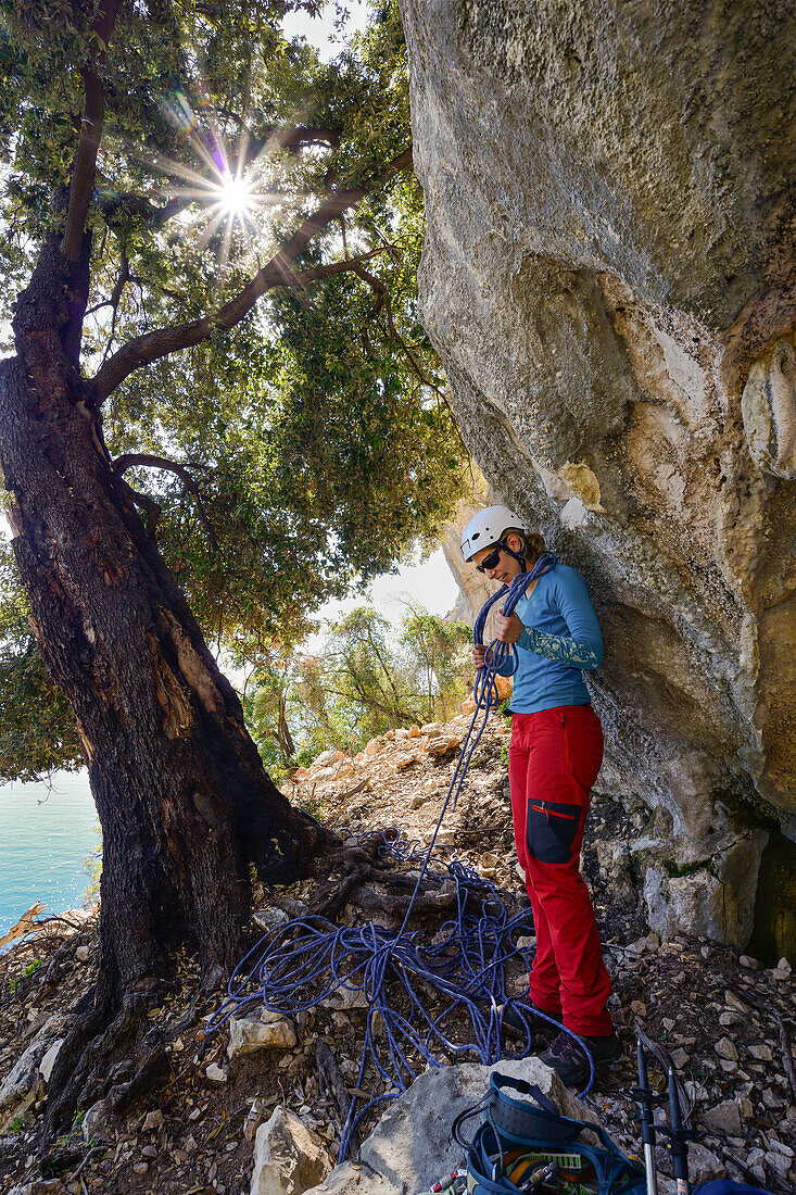 A young woman with climbing gear and a rope after abseiling in the mountainous coastal landscape above the sea, Golfo di Orosei, Selvaggio Blu, Sardinia, Italy, Europe