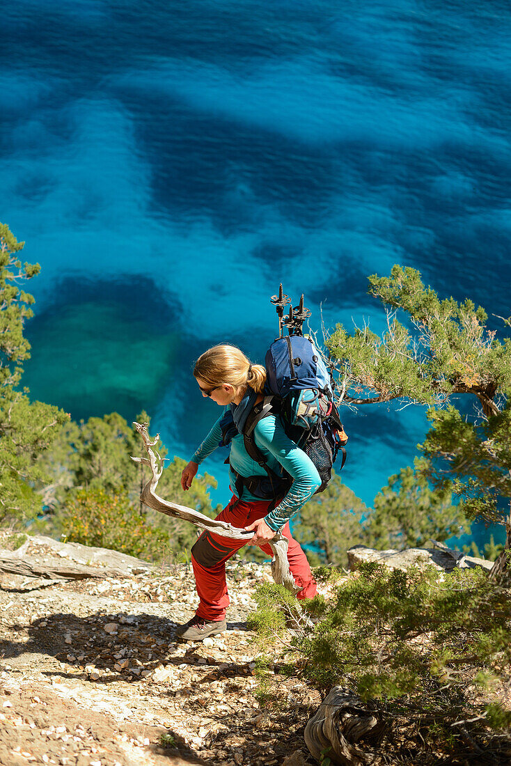 Eine junge Frau mit Trekkingausrüstung wandert oberhalb des Meeres entlang der gebirgigen Küste, Golfo di Orosei, Selvaggio Blu, Sardinien, Italien, Europa