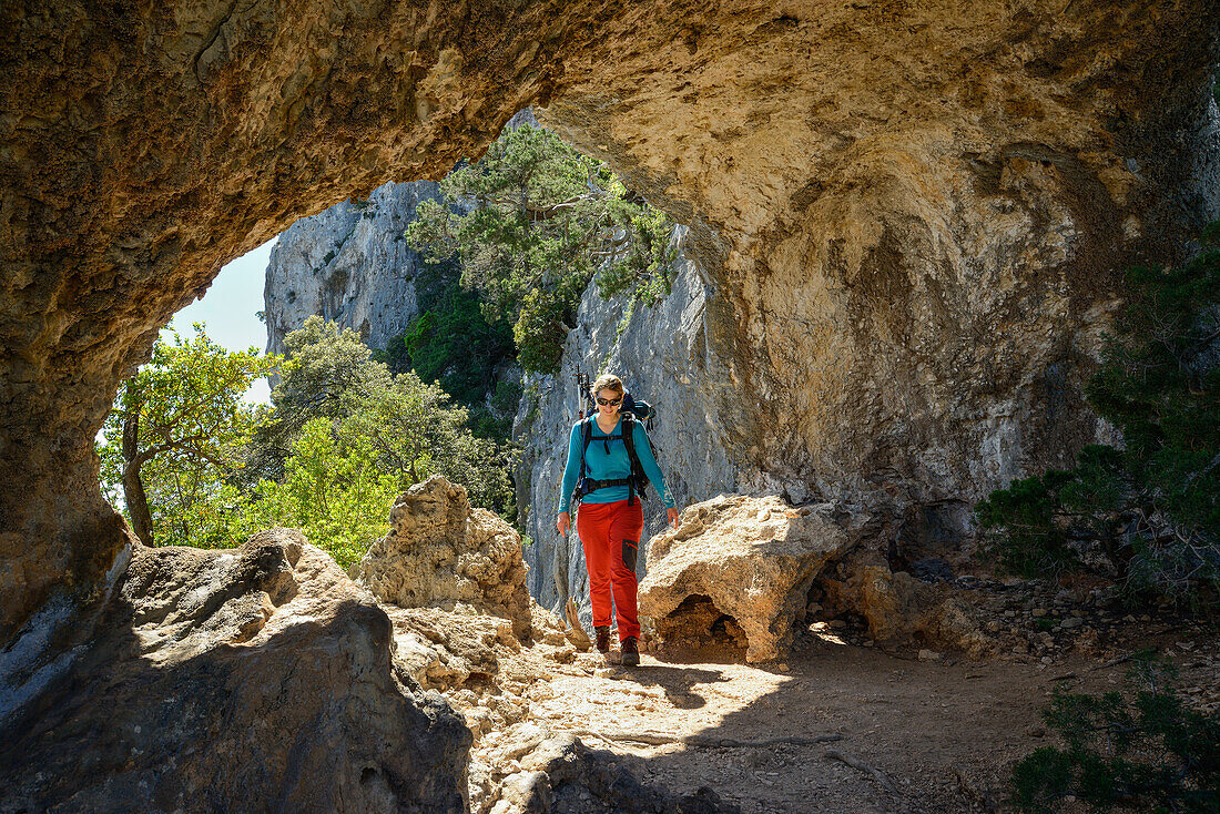 Eine junge Frau mit Trekkingausrüstung wandert durch den Felsbogen Arcu su Feilau oberhalb des Meeres entlang der gebirgigen Küste, Golfo di Orosei, Selvaggio Blu, Sardinien, Italien, Europa